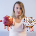 young woman choosing between donut and apple