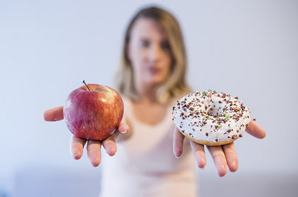 young woman choosing between donut and apple